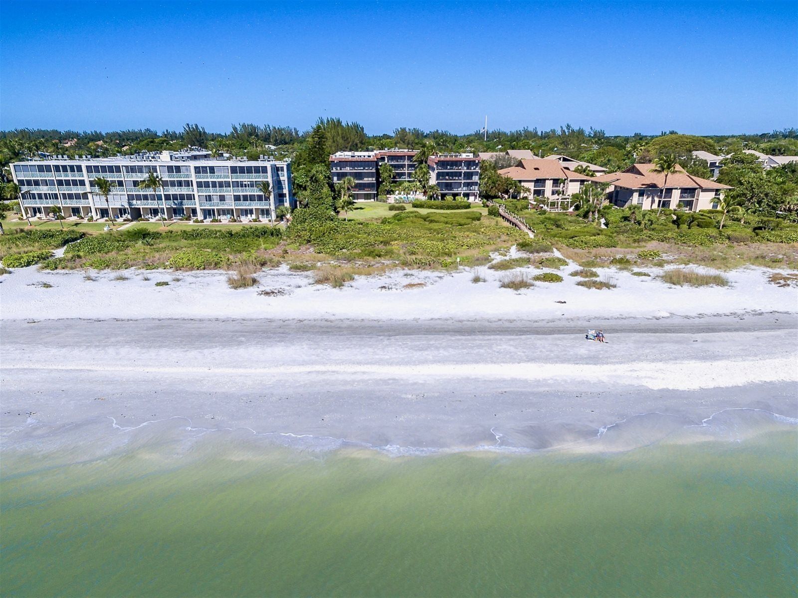 A beachfront hotel with multiple buildings, a sandy beach, and a clear blue sky.