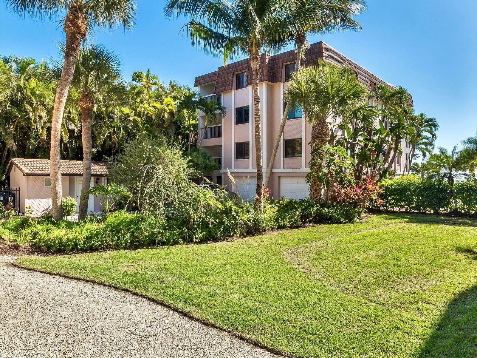 A multi-story building with a flat roof, surrounded by lush greenery and palm trees.