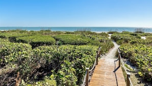 Une promenade en bois mène à une plage bordée de chaque côté d’une végétation luxuriante.