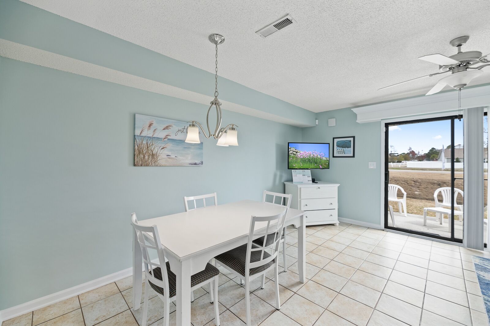 A dining area with a white table and chairs, a ceiling fan, and a television on a white cabinet.