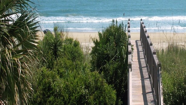 Une promenade en bois qui mène à une plage offrant une vue sur l’océan.