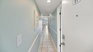 Un couloir aux murs bleu clair, doté d’un sol carrelé et d’une porte portant l’inscription « E1 ».