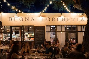 Ein Essbereich im Freien mit einem Schild mit der Aufschrift 'BUONA FORCHETTA' und einer sichtbaren Speisekarte.