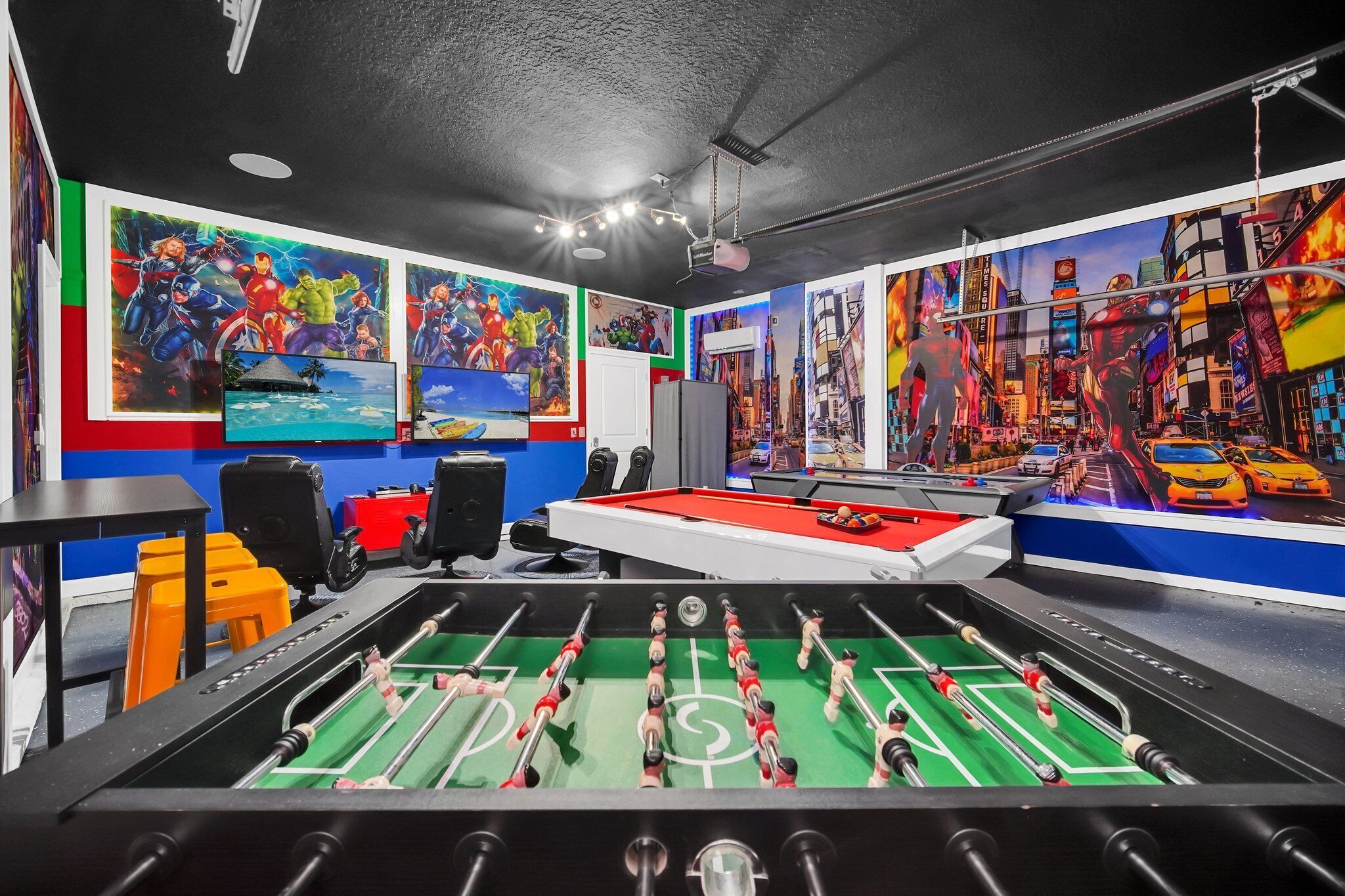 A room with a foosball table, a pool table, and vibrant murals on the walls.