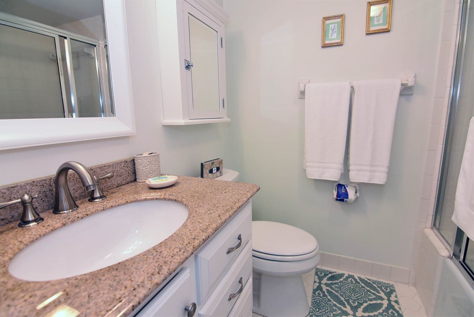 Une salle de bain avec un lavabo surmonté d’un plan de travail en granit, des toilettes blanches et un espace douche.