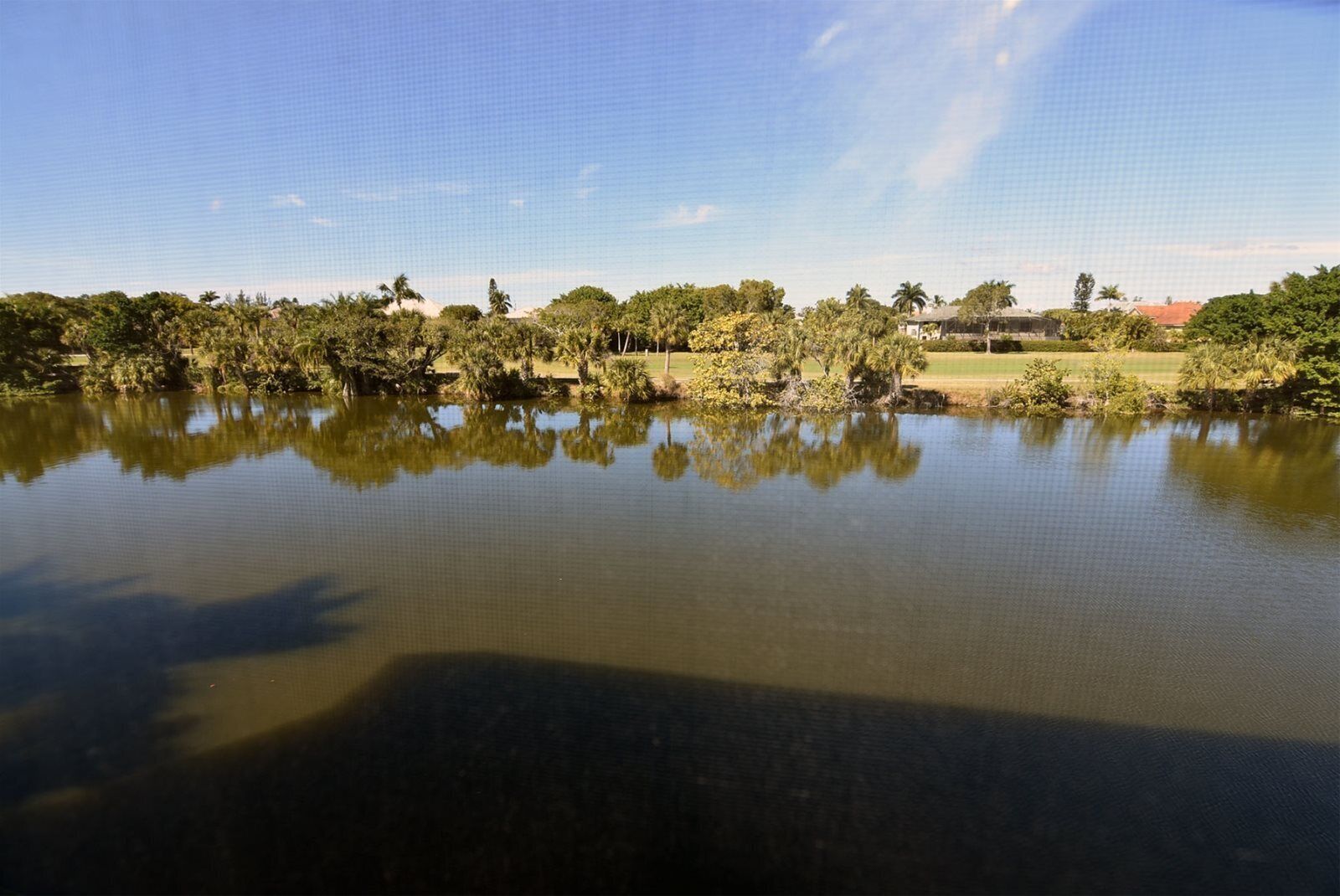Un llac tranquil amb reflexos d'arbres i un edifici allunyat.