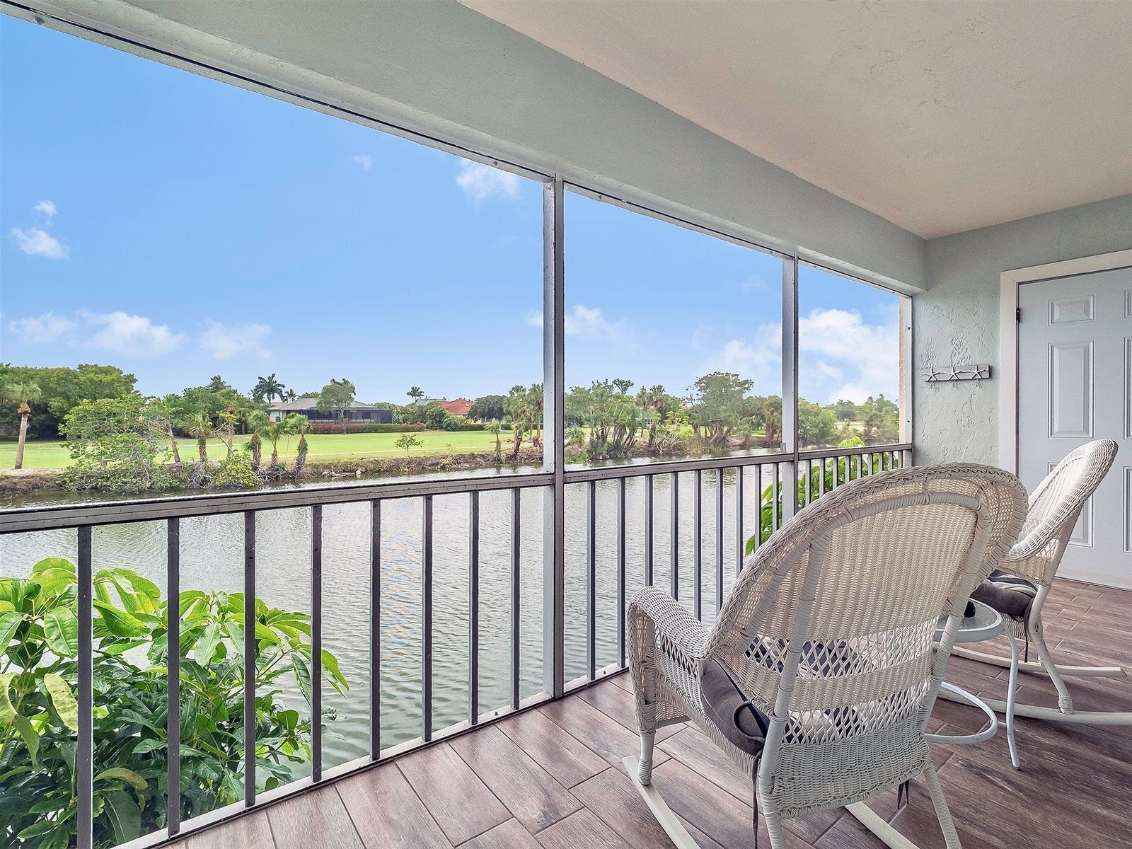 A balcony with wicker chairs, a view of a water body, and a grassy landscape.