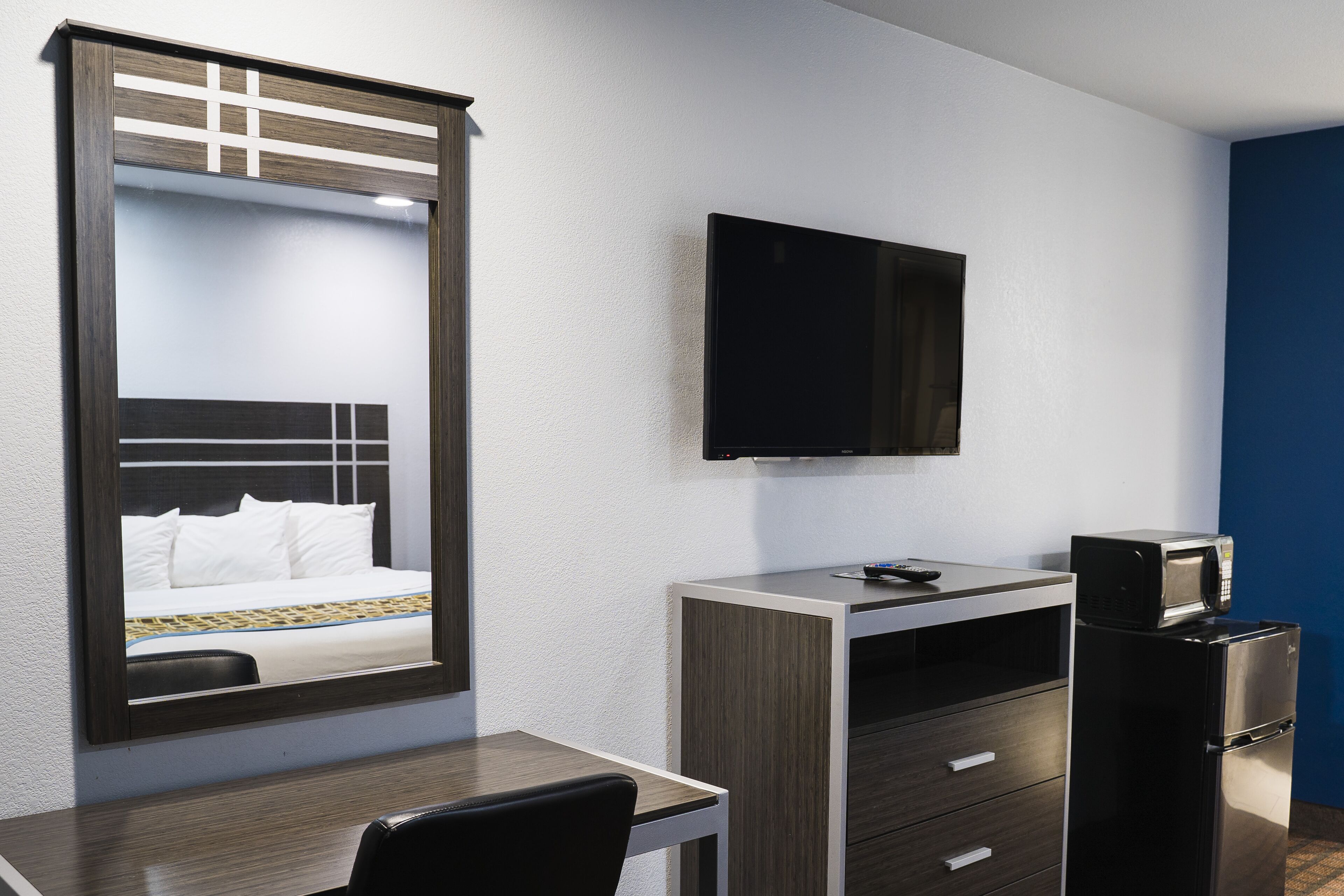 A hotel room with a bed, a desk, a television, and a refrigerator.
