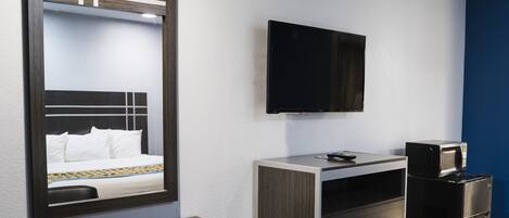 A hotel room with a bed, a desk, a television, and a refrigerator.