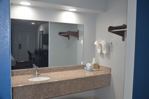 A bathroom with a granite countertop sink, a mirror, and a towel rack. - Traveler's Inn (Rosenberg)
