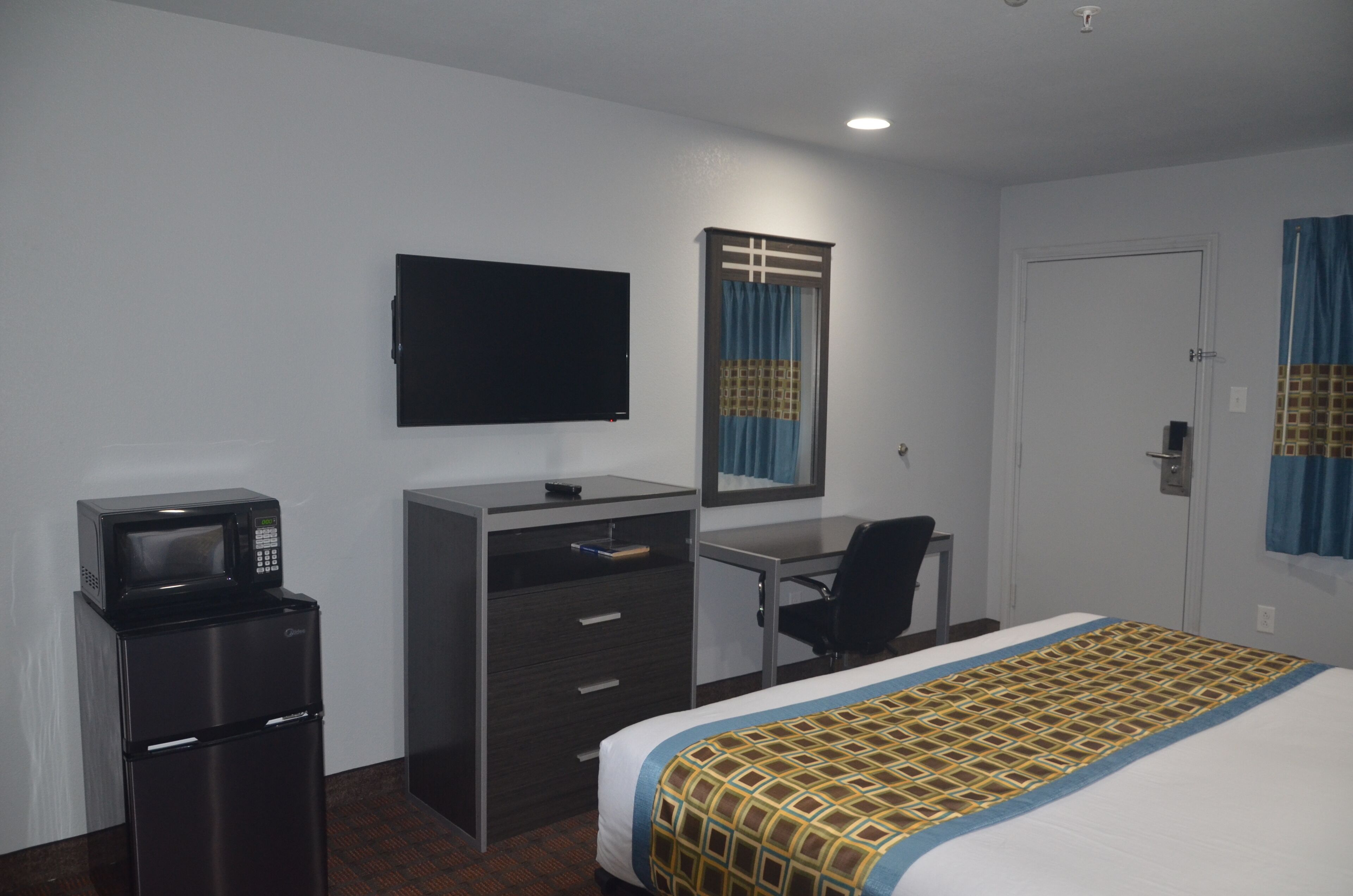 A hotel room with a bed, a desk, a chair, a television, a microwave, and a refrigerator.