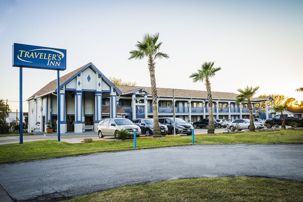A Traveler's Inn with a two-story building, a parking lot, and several palm trees. - Traveler's Inn (Rosenberg)