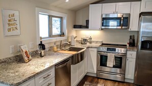 A modern kitchen with stainless steel appliances, a granite countertop, and white cabinetry. - Traveler's Mountain Retreat w/ Grotto Cave Room (Idaho Springs)