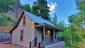 A single-story house with a porch, stone foundation, and a metal roof. - Traveler's Mountain Retreat w/ Grotto Cave Room (Idaho Springs)