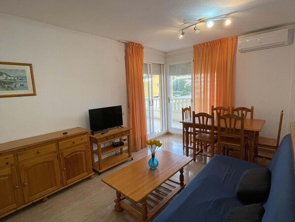 A living room with a TV, wooden furniture, a sofa, and a dining table.