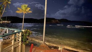 A nighttime beach scene with a clear view of the ocean, palm trees, and a wooden walkway leading to the water.