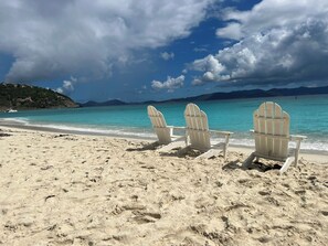 A beach with three Adirondack chairs facing the ocean.