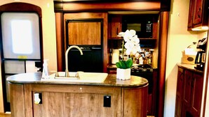 A kitchen with a wooden island, stainless steel sink, and a microwave. - Cactus Camper has lake views with dock & lake access (Spicewood)