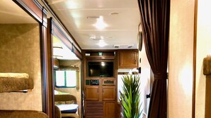 A compact RV interior with a dining area, kitchenette, and a large window with curtains. - Cactus Camper has lake views with dock & lake access (Spicewood)