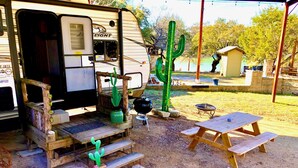 A recreational vehicle with a small deck, a cactus, a grill, and a picnic table. - Cactus Camper has lake views with dock & lake access (Spicewood)