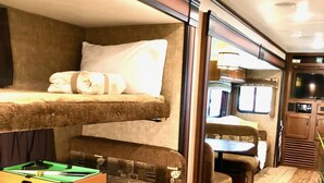 A compact RV interior with a bunk bed, a small table with a pool table, and a kitchenette area. - Cactus Camper has lake views with dock & lake access (Spicewood)