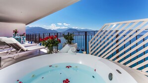 En balkon med jacuzzi, liggestole og et bord med blomster.