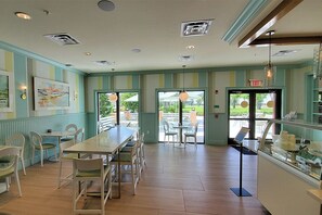 Interior de restaurant amb parets amb ratlles, una taula llarga amb cadires, llums penjants i vistes per les finestres.