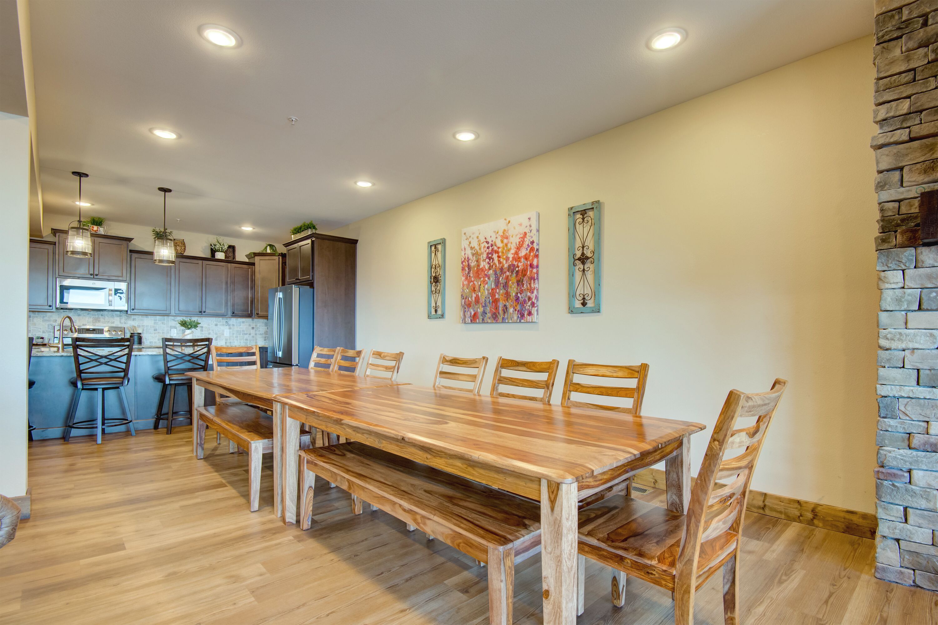 A spacious dining area with a wooden table and benches, a kitchen with modern appliances, and a stone accent wall.