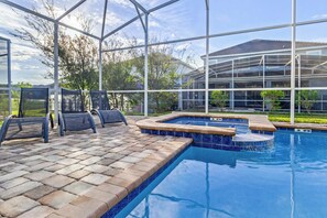 An indoor swimming pool with a tiled deck, seating area, and a glass enclosure.