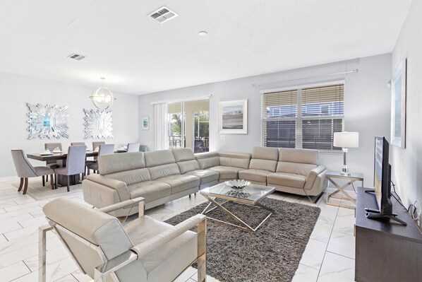 A modern living room with a sectional sofa, a glass coffee table, and a dining area with a table and chairs.
