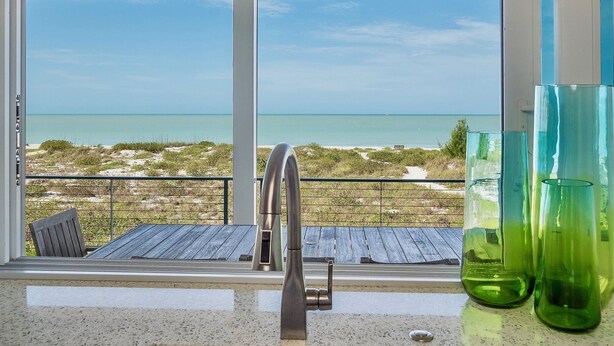 Una cocina con vistas a la playa, un grifo de acero inoxidable y dos jarrones de vidrio verde.
