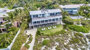 Un inmueble frente a la playa con varias plantas, piscina, palmeras y vista al océano.