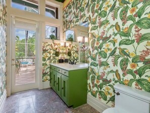 A bathroom with floral wallpaper, a green vanity, and a window overlooking a patio. - Bougainvillea Home (Captiva)