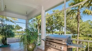 A patio with a stainless steel grill, potted plants, and a view of palm trees and a body of water. - Bougainvillea Home (Captiva)