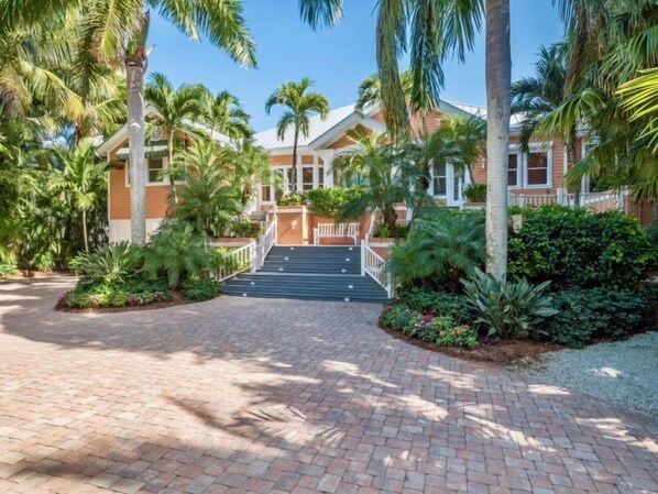 A hotel entrance with a brick pathway leading to a set of stairs, surrounded by lush greenery and palm trees. - Bougainvillea Home (Captiva)