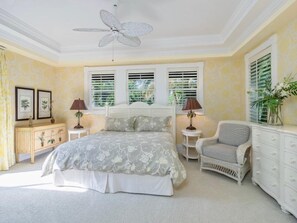 A bedroom with a bed, two bedside tables, a chair, a dresser, and a ceiling fan. - Bougainvillea Home (Captiva)