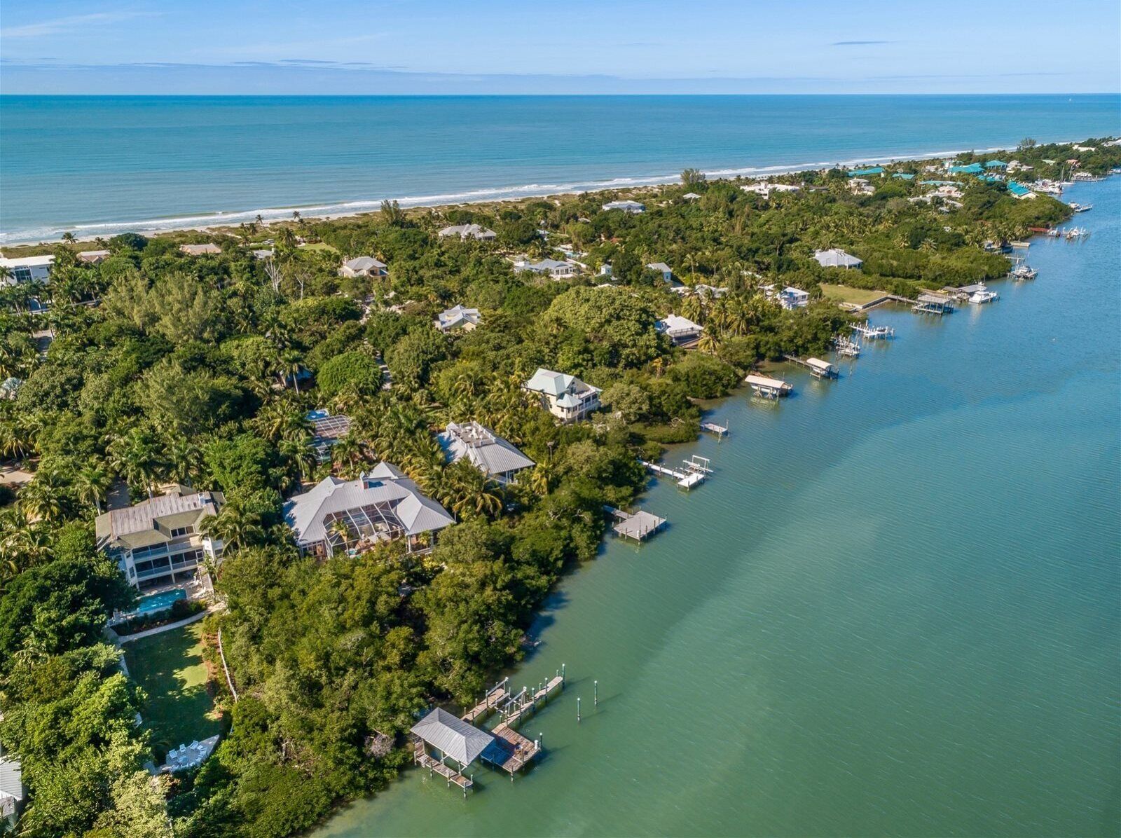 An aerial view of a coastal residential area with houses, docks, and a clear view of the ocean.
