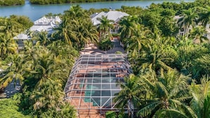 A resort with a glass-enclosed pool, surrounded by palm trees and a view of the water. - Bougainvillea Home (Captiva)