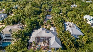 An aerial view of a coastal residential area with houses surrounded by dense tropical vegetation and a clear view of the ocean. - Bougainvillea Home (Captiva)