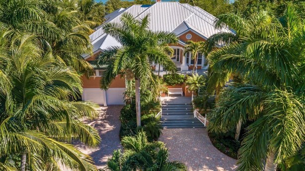 A large house with a covered porch, surrounded by lush greenery and a view of a calm body of water. - Bougainvillea Home (Captiva)