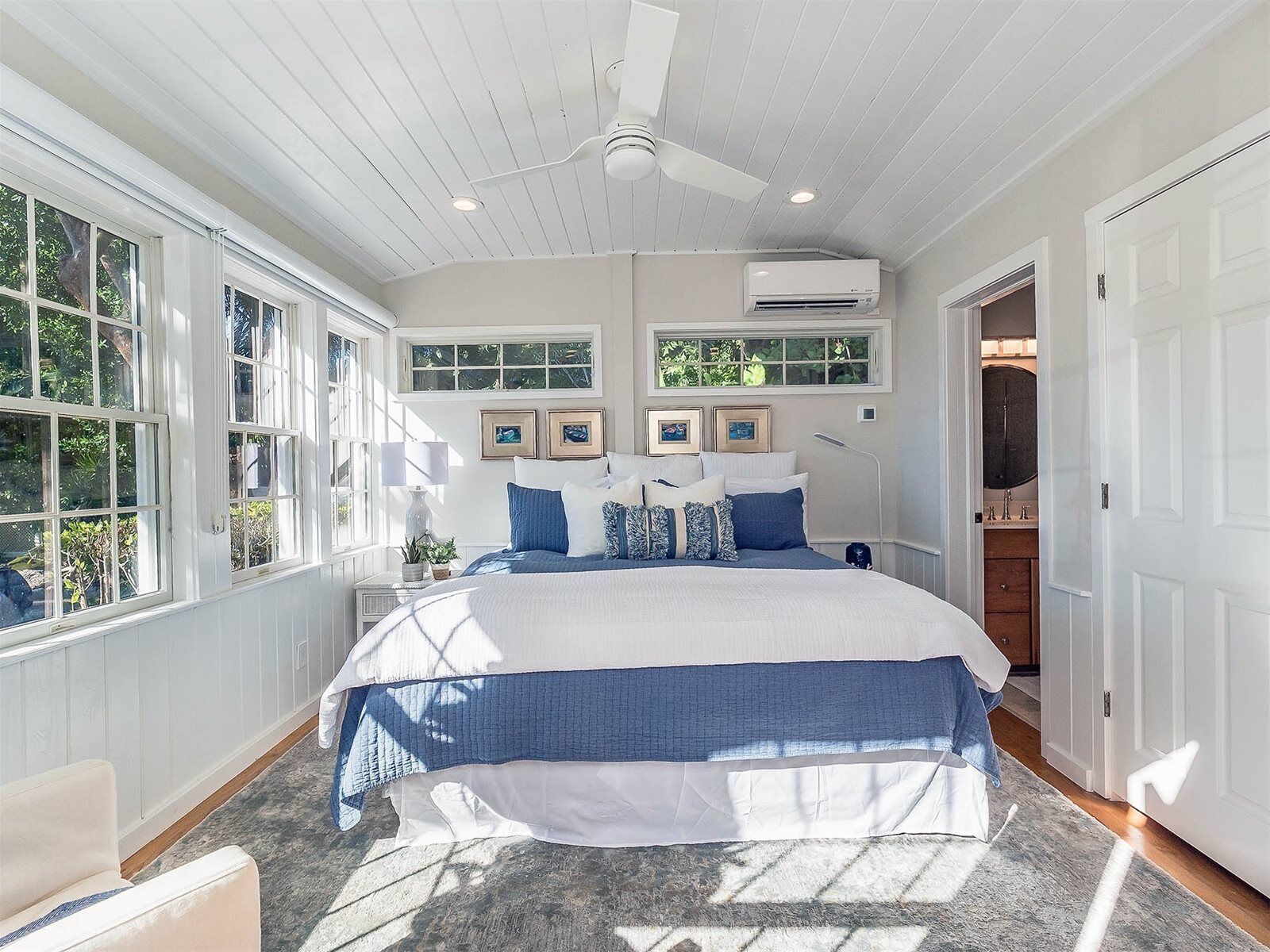A bedroom with a large bed, two windows, an air conditioning unit, and a ceiling fan.