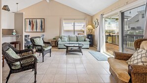 A spacious living area with wicker furniture, a glass coffee table, and a sliding glass door leading to a balcony. - The Shell Shack (Galveston)