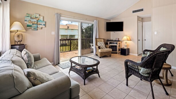 A living room with a sofa, wicker chairs, a glass coffee table, and a flat-screen TV. - The Shell Shack (Galveston)