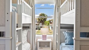 A room with two bunk beds, a small table with a lamp, and a window with curtains. - The Shell Shack (Galveston)