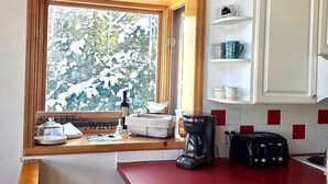 Una cocina con vista a árboles cubiertos de nieve por la ventana, una cafetera y un tostador en la encimera.