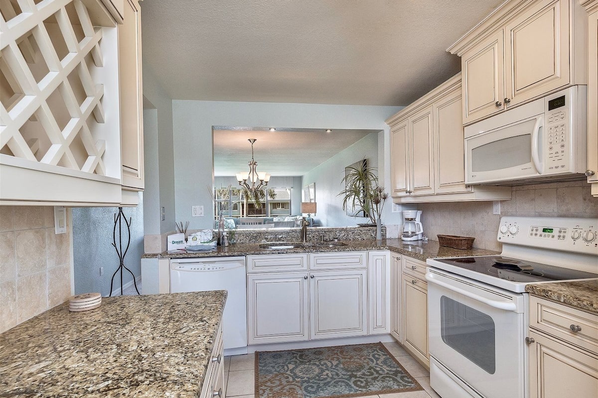 A kitchen with white cabinetry, a granite countertop, a dishwasher, a stove, and a microwave.