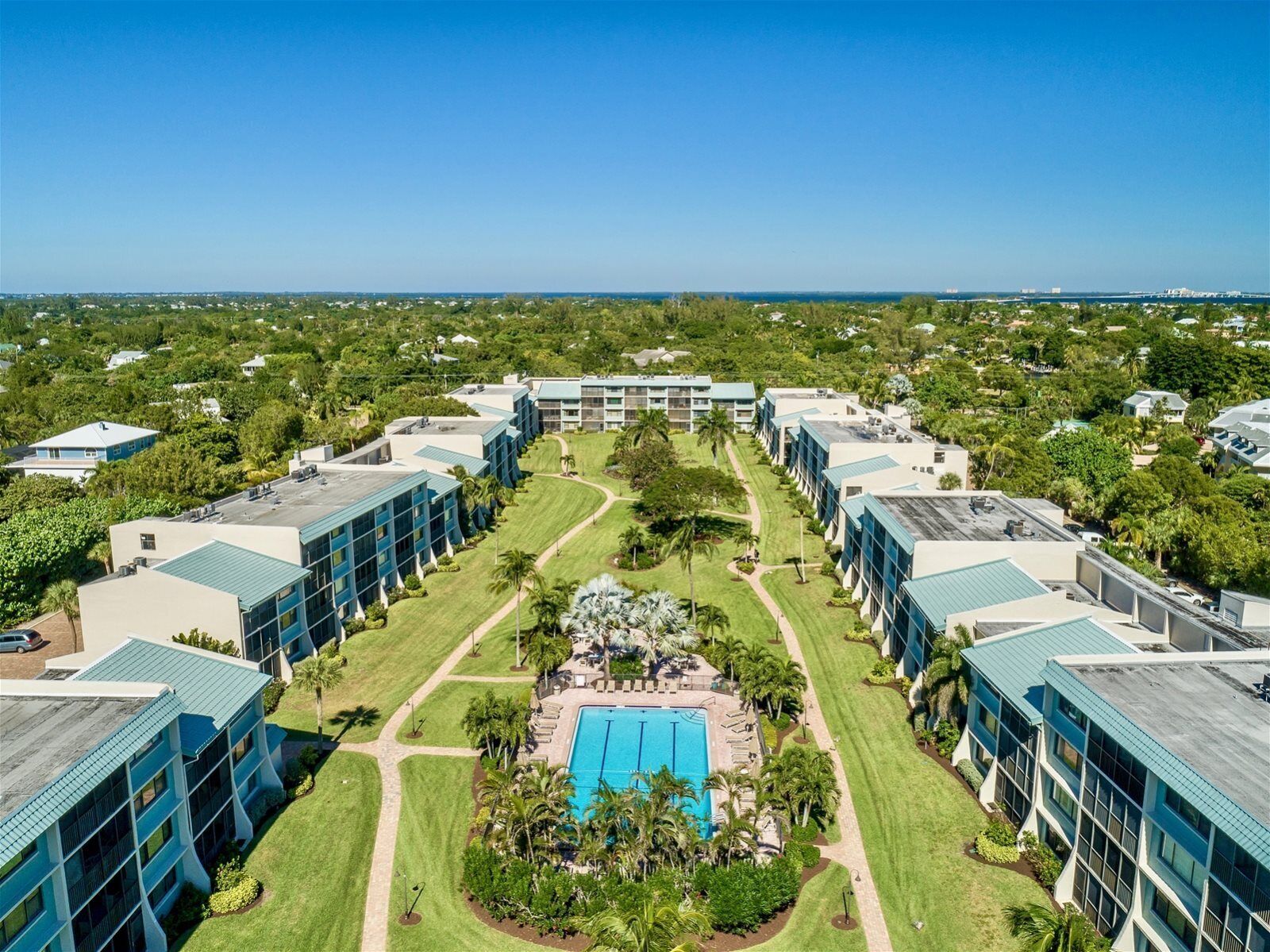 Un hotel moderno con una piscina centrale, circondato da prati curati e palme.
