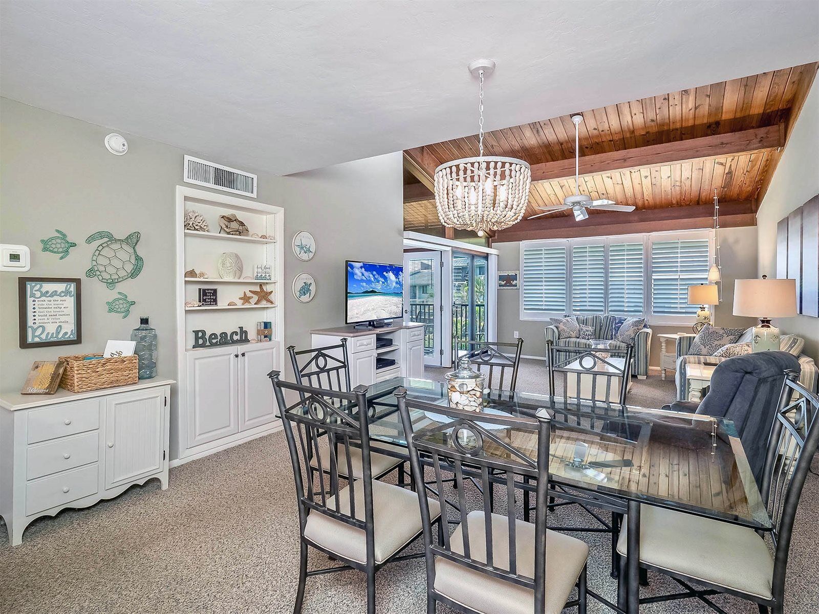 A spacious living room with a glass dining table, modern furniture, a large TV, and a view of the outdoors.