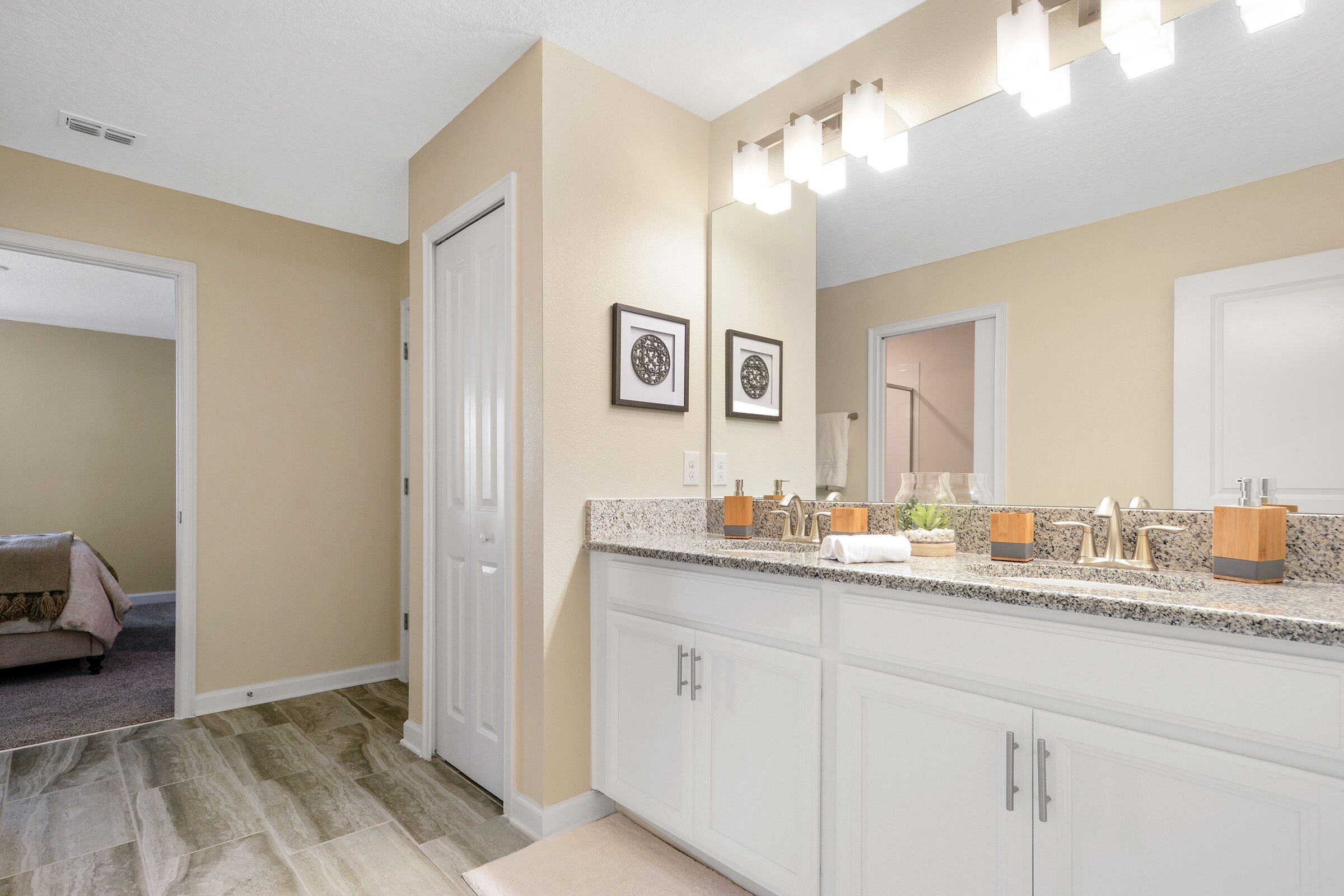 Un baño moderno con un espejo grande, armarios blancos y encimera de granito.