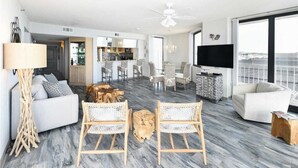 Un soggiorno moderno con un divano, due poltrone in vimini, un tavolino da caffè e una TV. Si vede anche un'area pranzo con tavolo e sedie, e una cucina sullo sfondo.